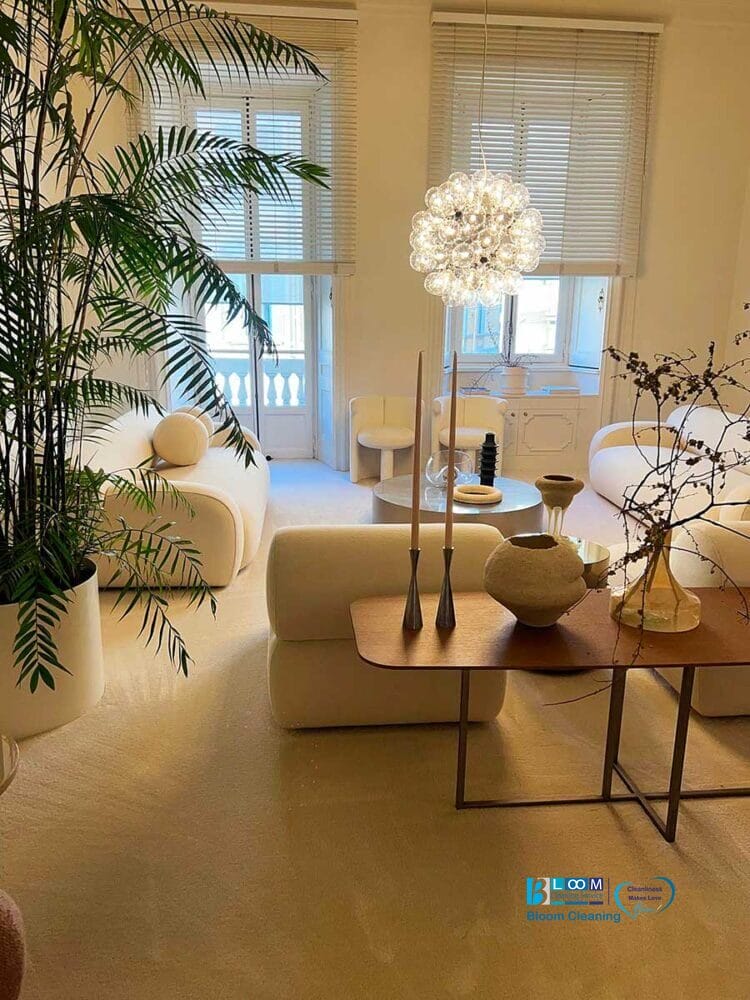 Soggiorno moderno con mobili bianchi, grandi piante e un lampadario unico, illuminato dolcemente dalla luce naturale: ideale per chi cerca pulizia moquette zona Amendola o pulizia moquette Milano.