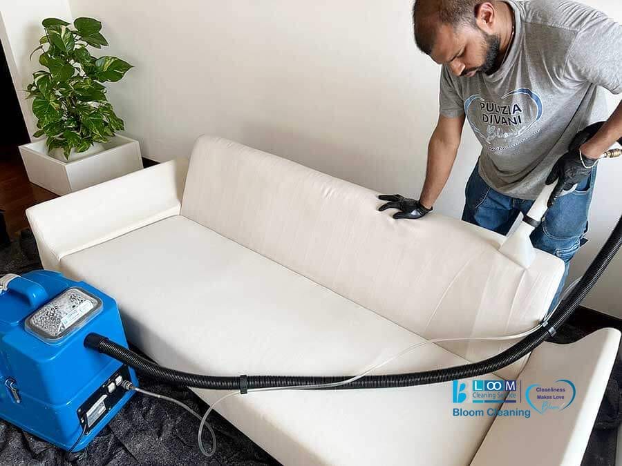 Un uomo usa un aspirapolvere per pulire un divano bianco in un soggiorno, a dimostrazione dei servizi professionali di lavaggio divani domicilio Monza.