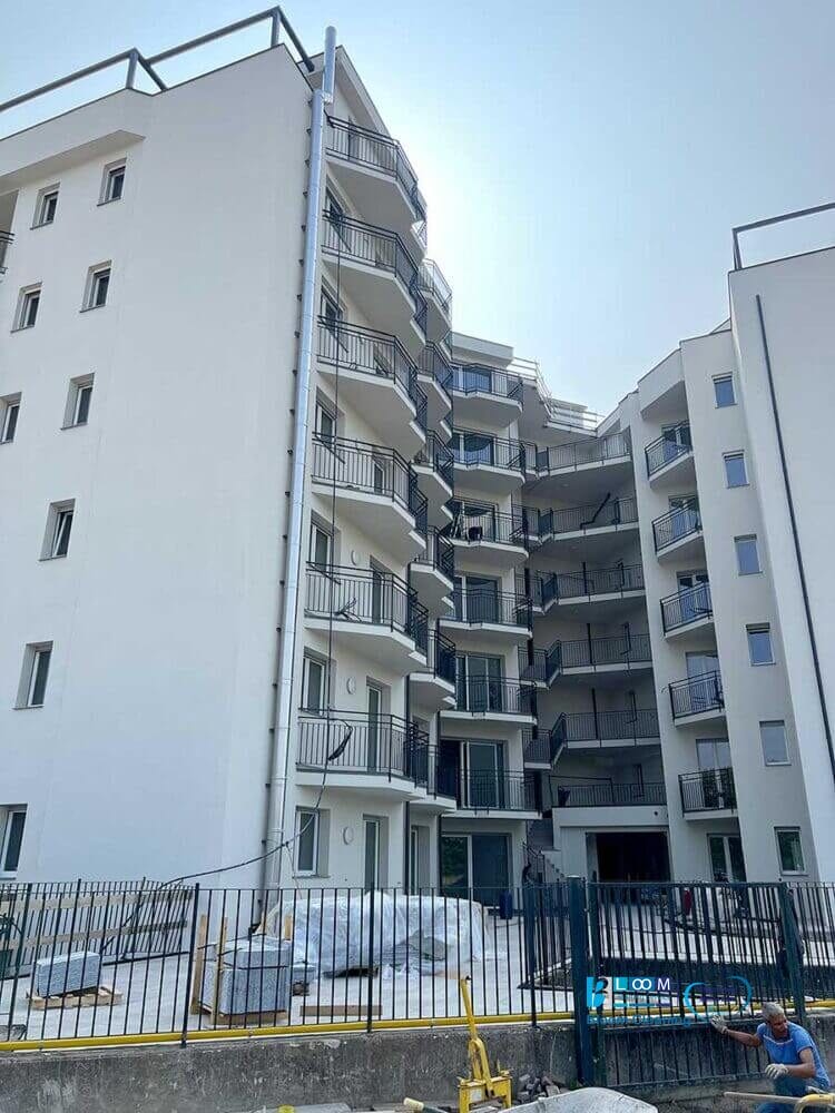 Un moderno condominio bianco a più piani con balconi e un'area recintata antistante, sotto un cielo limpido, che mette in mostra i risultati impeccabili della pulizia post cantiere Nerviano.