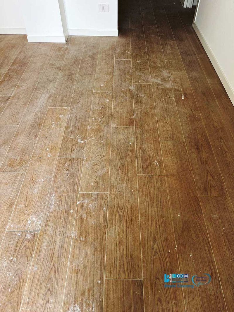 Pavimento in piastrelle effetto legno con schizzi di vernice bianca sparsi in una stanza vuota con pareti bianche, ideale per mettere in mostra i servizi di pulizia post cantiere Nerviano.