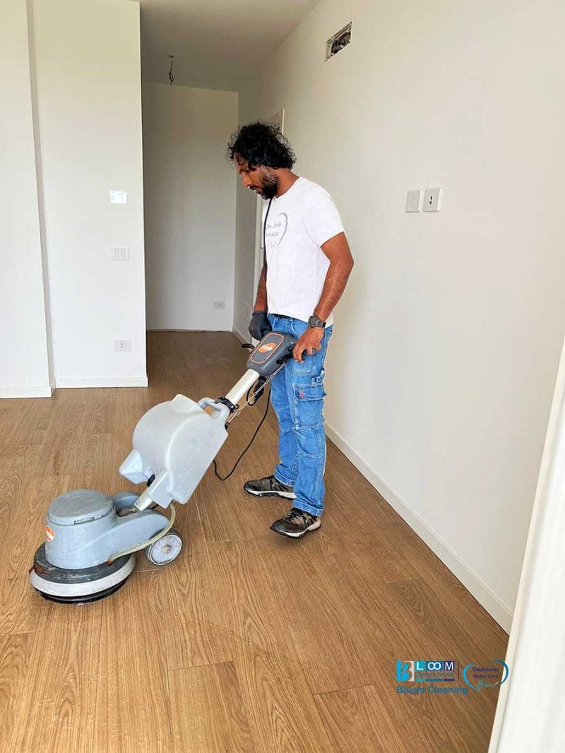 Uomo che esegue la pulizia post cantiere Nerviano, pulendo un pavimento in legno con una lucidatrice in una stanza luminosa e vuota.