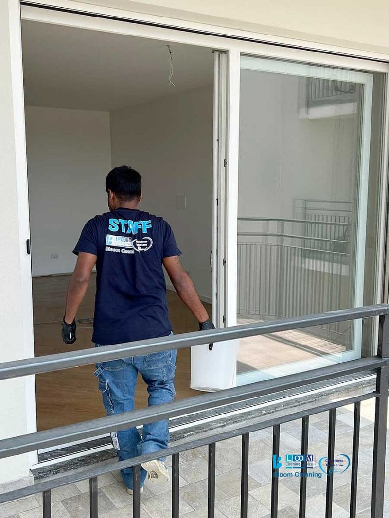 Una persona che indossa guanti e una maglietta con la scritta "STAFF" trasporta un secchio in una stanza vuota e senza arredi, pronta per la pulizia post cantiere Nerviano.