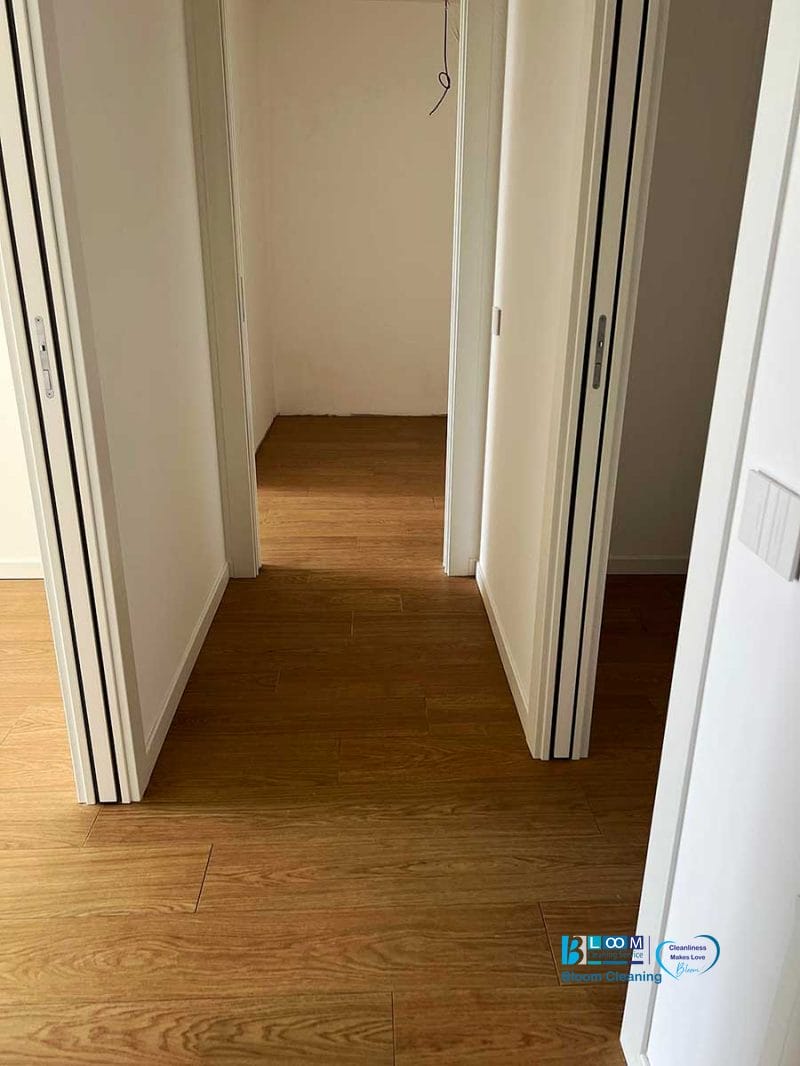 Vista di un corridoio con pavimento in legno, pareti bianche e due porte aperte che conducono a stanze vuote dopo la pulizia post cantiere Nerviano.