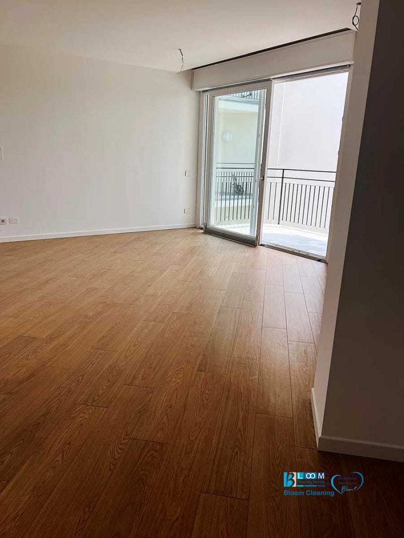 Stanza vuota con pavimento in legno, pareti bianche e porte scorrevoli in vetro che conducono a un balcone con ringhiera: ideale per mostrare i risultati della pulizia post cantiere Nerviano.