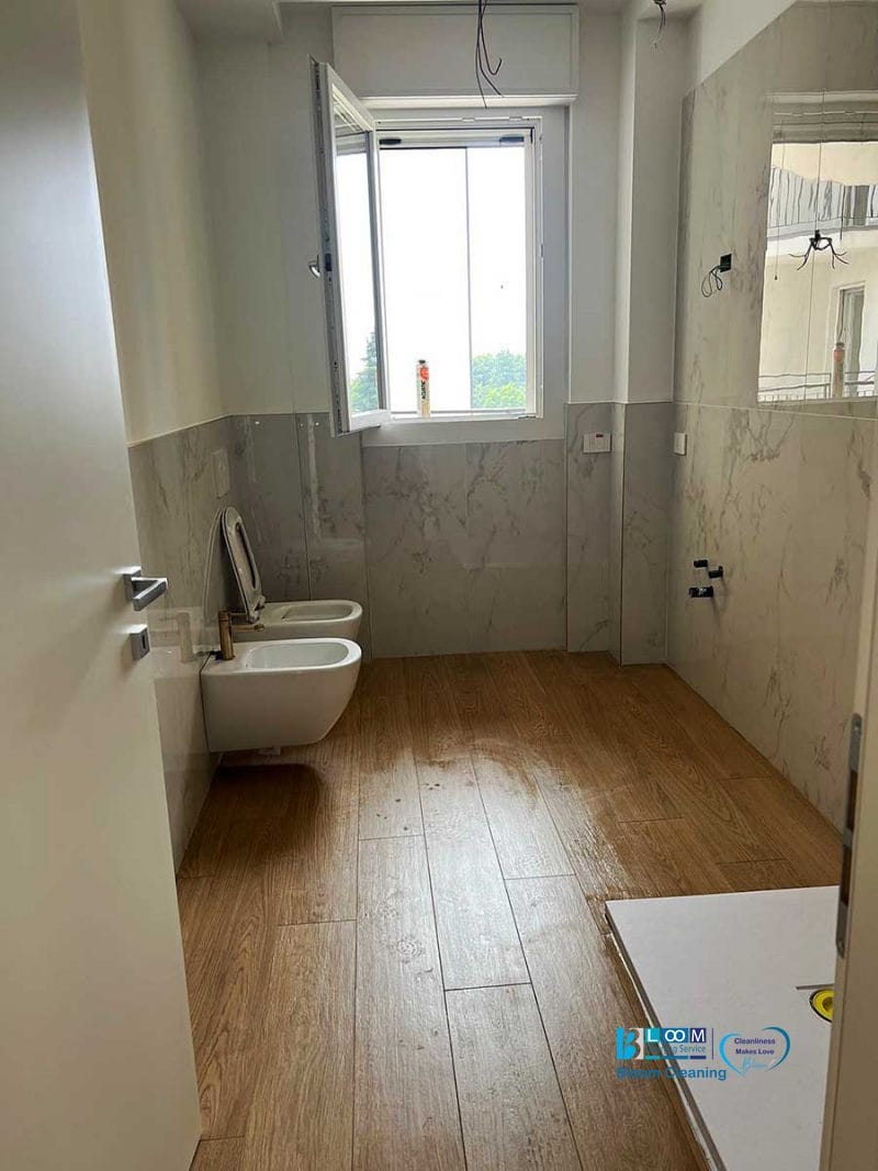 Bagno con pavimento effetto legno, pareti bianche, finestra aperta, WC, bidet e zona doccia non rifinita: perfetto per una pulizia post cantiere Nerviano per restituire freschezza dopo la ristrutturazione.