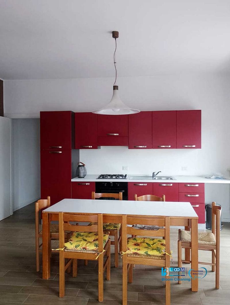 Cucina moderna con mobili rossi, un tavolo bianco e sei sedie in legno con cuscini gialli a fiori: perfetta per chi apprezza lo stile e la comodità della pulizia appartamenti Bollate.