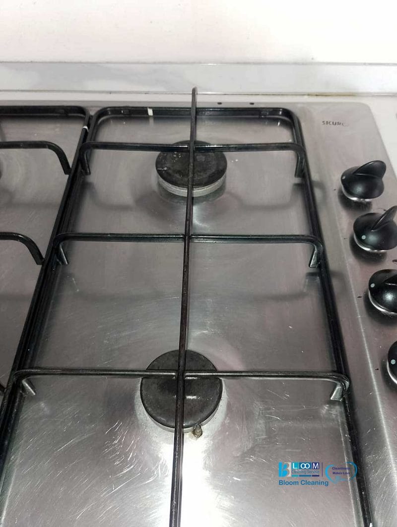Una cucina a gas in acciaio inox con due fuochi e manopole di controllo nere sul lato destro, perfetta per cucine moderne o pulizia appartamenti Bollate.