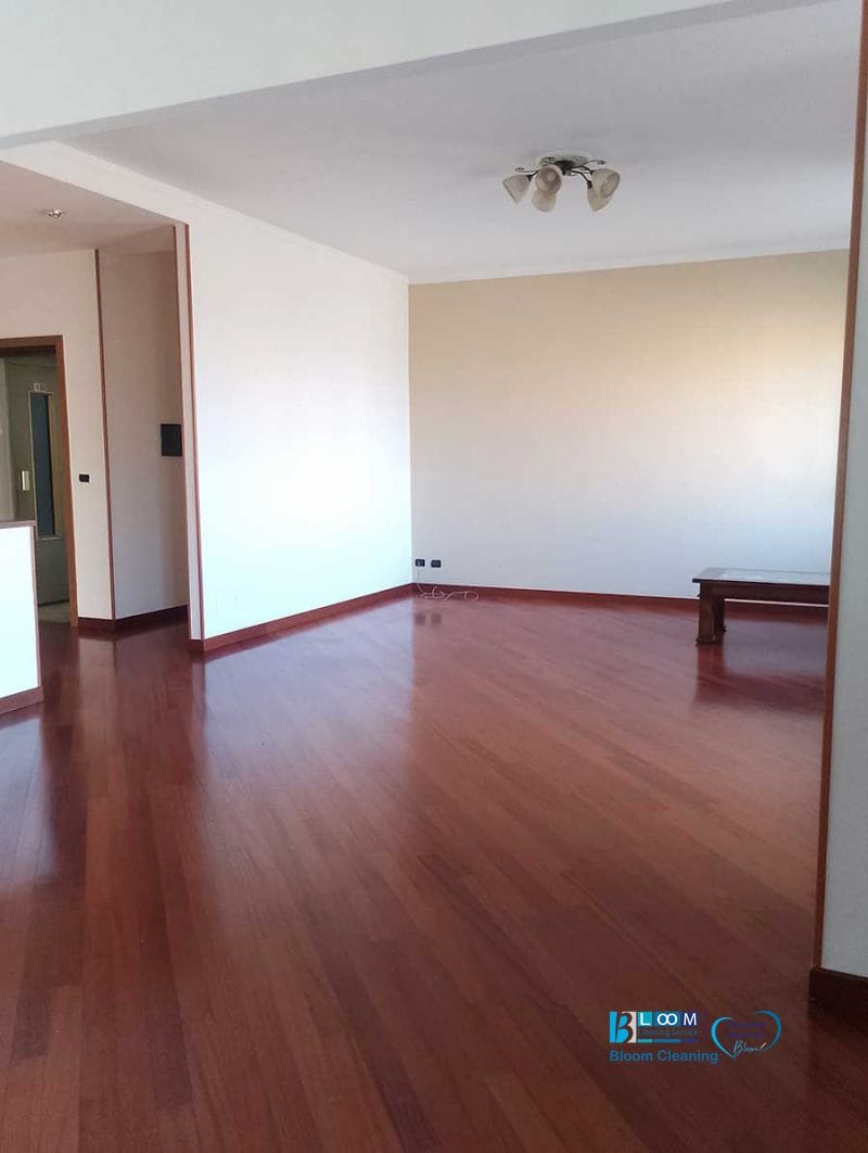 Ampia stanza vuota con pavimento in legno, pareti bianche, lampada a soffitto e una piccola panca nell'angolo: perfetta per chi cerca pulizia appartamento Novate Milanese.