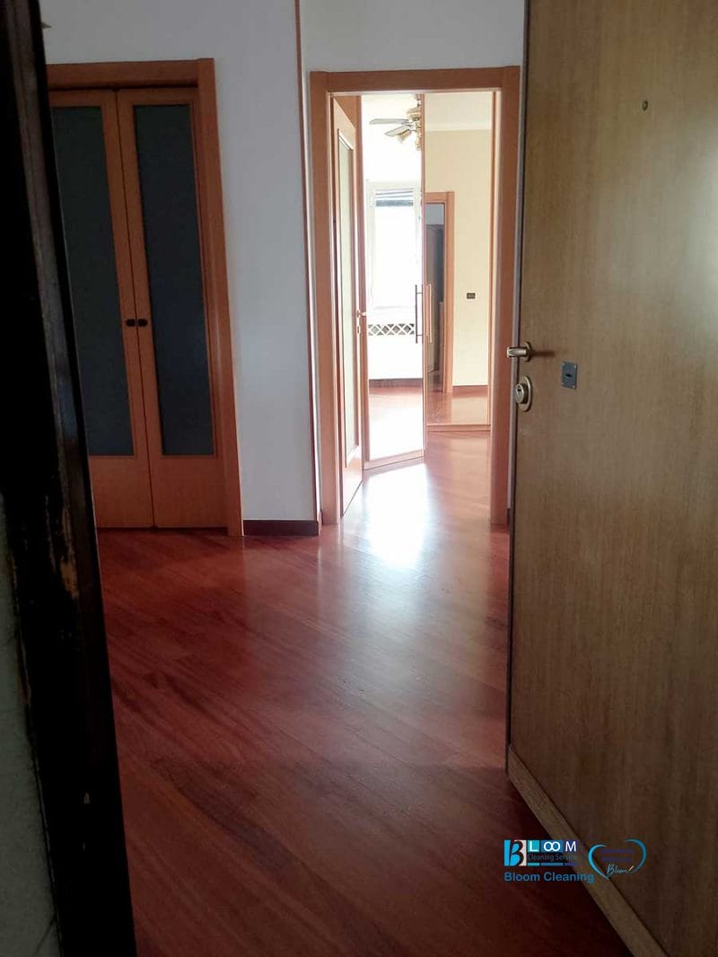 Un corridoio con pavimenti in legno, porte aperte e luce solare proveniente da una stanza in fondo: ecco i risultati della pulizia dell'appartamento Novate Milanese.