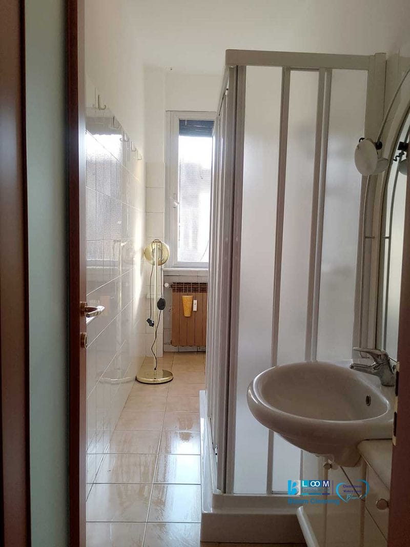 Bagno stretto con doccia, piccolo lavandino e una finestra in fondo che lascia entrare la luce naturale: perfetto per chi cerca pulizia appartamento Novate Milanese.