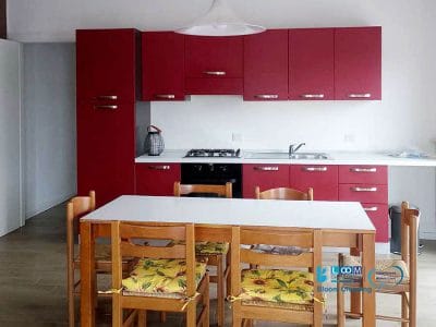 Cucina moderna con mobili rossi, piano di lavoro bianco e tavolo da pranzo in legno con sedie, mantenuta alla perfezione da pulizia appartamenti Bollate.