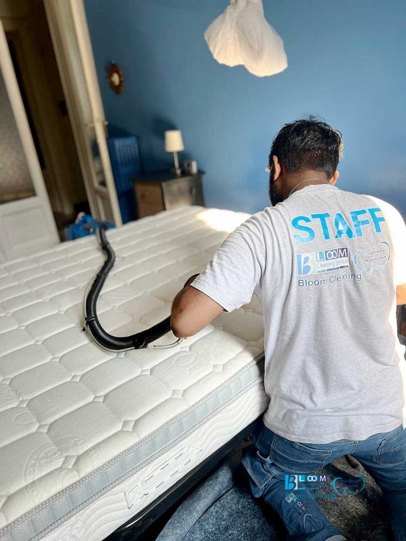 Un'operatrice in camicia da lavoro esegue il Lavaggio Materassi, utilizzando un tubo di aspirazione per Igiene Profonda su un materasso in una camera da letto.