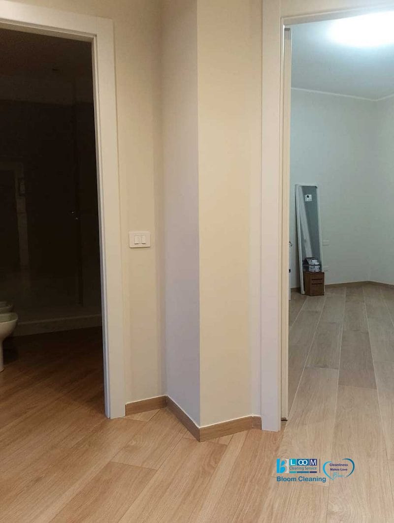 Un corridoio con due porte che si aprono su stanze separate, con pavimenti in legno chiaro e pareti beige dopo una recente imbiancatura appartamento Corsico per un look rinnovato e moderno.