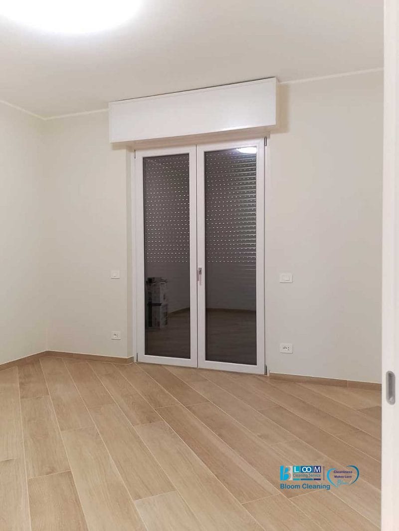 Stanza vuota con pavimento in legno chiaro, pareti bianche e porte in vetro chiuse con una serranda - ideale per chi cerca un servizio sgombero e imbiancatura o pulizia post-imbiancatura professionale dopo lavori di rinnovo.
