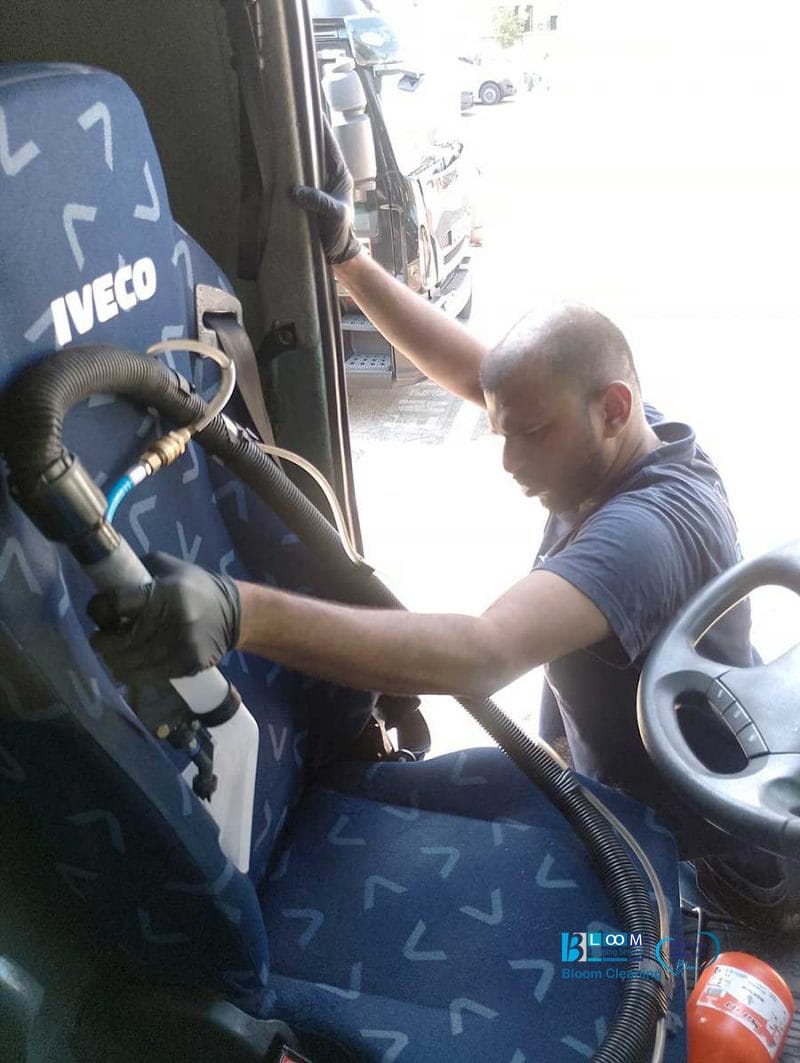 Un uomo con i guanti sta pulendo con l'aspirapolvere un sedile di un veicolo Iveco blu, specializzato in pulizia sedili furgoni Milano per risultati professionali e approfonditi.