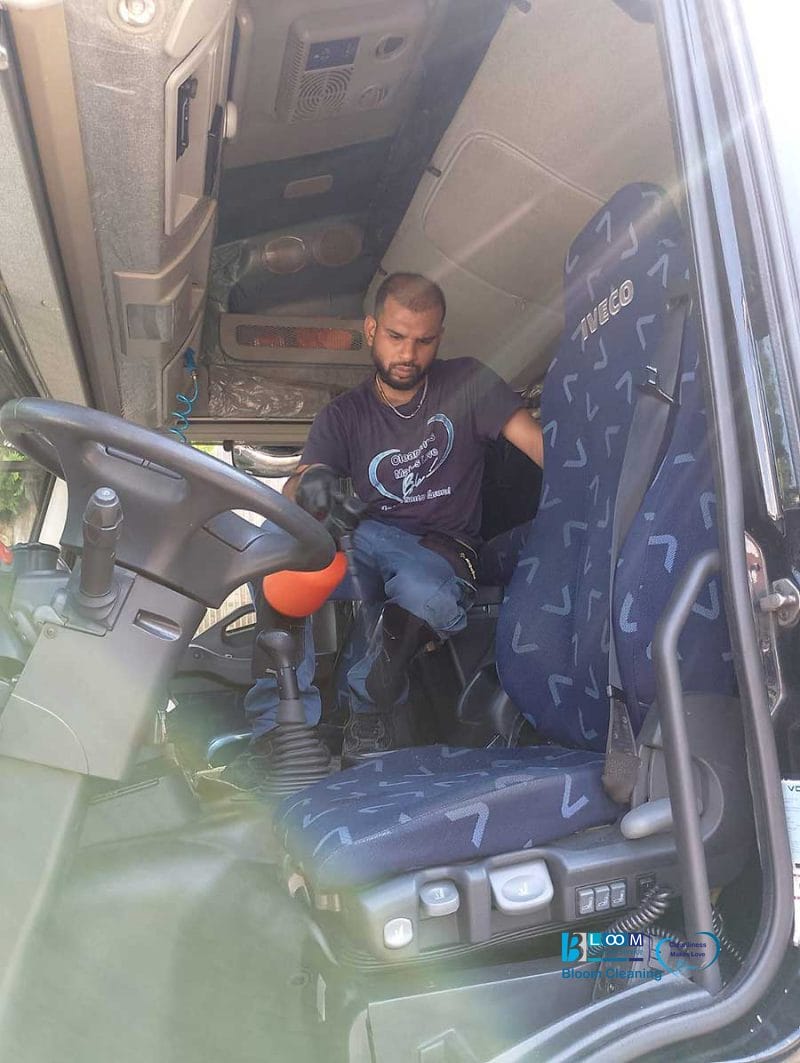 Un uomo si trova all'interno della cabina di un camion, regolando qualcosa vicino al sedile del conducente in una giornata di sole, forse preparandosi per la pulizia sedili furgoni Milano o altri servizi di lavaggio interni mezzi aziendali Milano.