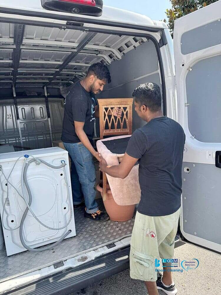 Due uomini caricano una lavatrice e una sedia sul retro di un furgone bianco in una giornata di sole, gestendo con cura il trasporto mobili a Milano.