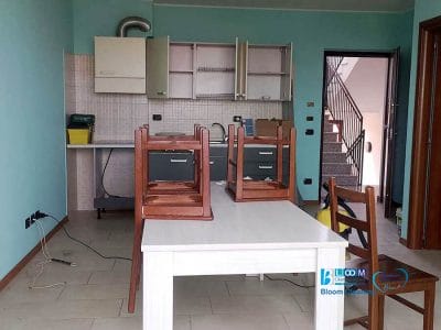 Piccola cucina con due sedie capovolte su un tavolo bianco, ante di armadietti aperti e una scala sullo sfondo: ideale per una pulizia post trasloco crema o per l'intervento di un'impresa pulizie appartamenti crema.