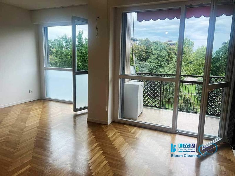 Camera vuota e luminosa con pavimento in parquet, finestre aperte e vista sugli alberi e sul balcone esterno, ideale per la pulizia post ristrutturazione Milano 2 per far risplendere ogni angolo.