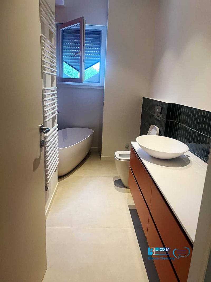 Bagno moderno con vasca freestanding e lavandino a vaschetta, splendente dopo una pulizia post ristrutturazione Milano 2, con luce naturale che filtra dalla finestra aperta.