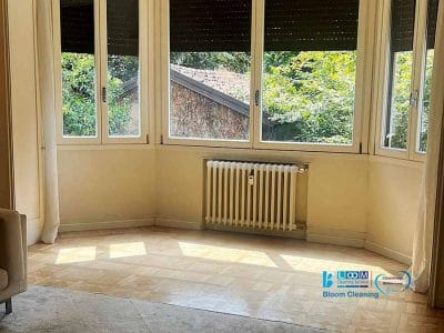 Camera luminosa con ampie finestre, radiatore sottostante, luce solare sul pavimento in parquet e vista sugli alberi all'esterno: ideale per la pulizia generale appartamento Affori per mantenerla fresca e invitante.