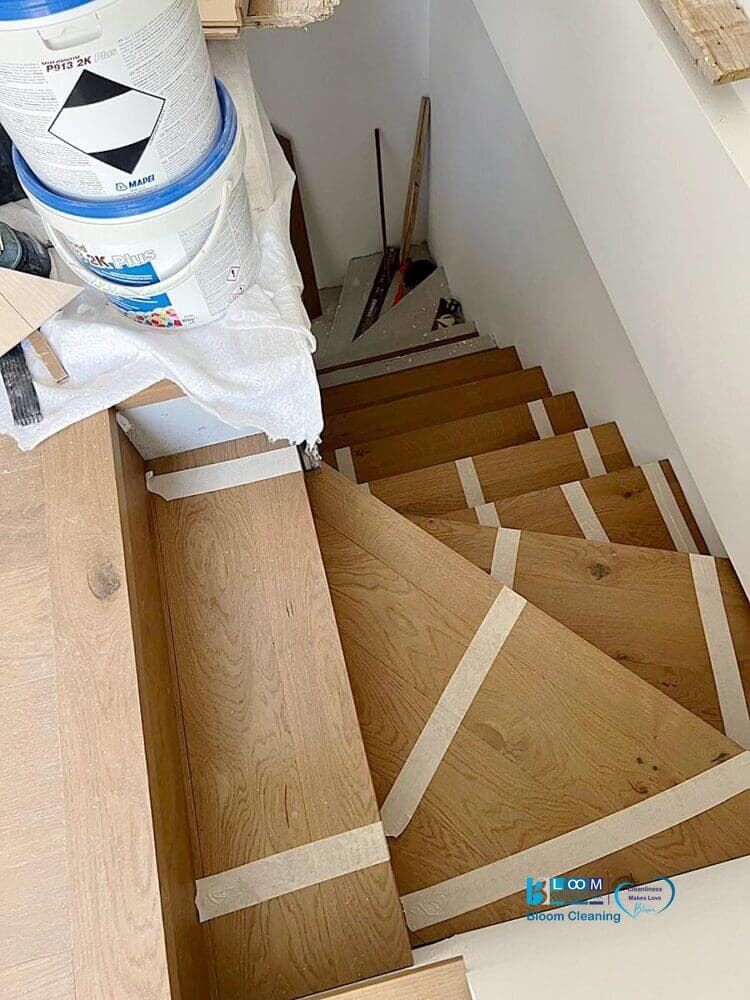 Scale in legno in fase di ristrutturazione in Lombardia, con nastro adesivo sui gradini, materiale di verniciatura nelle vicinanze, e pronte per pulizie finali cantiere in nuovi appartamenti.
