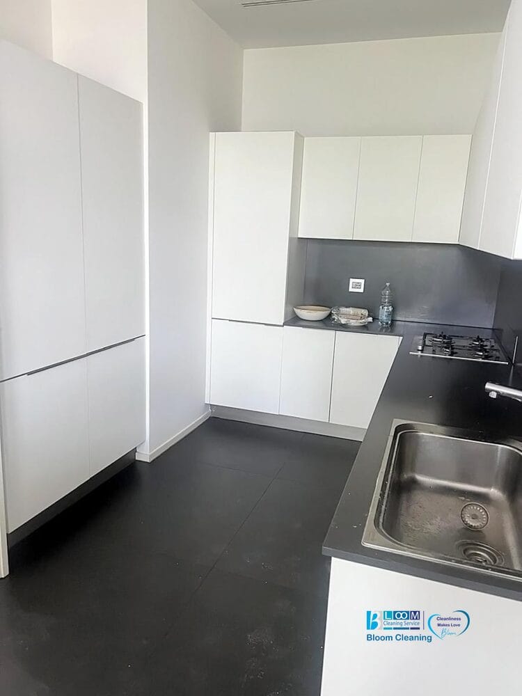 Cucina moderna con armadietti bianchi, piani di lavoro neri e un aspetto impeccabile, ideale per chi cerca pulizia post sgombero appartamento Milano o smaltimento mobili ingombranti Milano in uno spazio pulito e minimalista.
