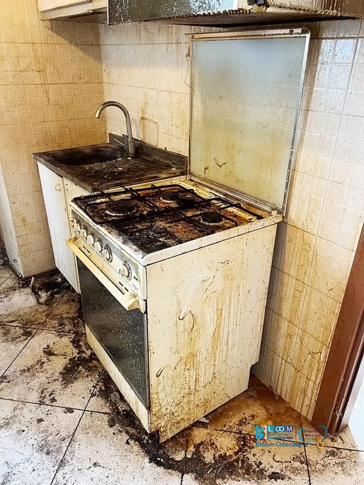 Una cucina sporca con fornelli macchiati, superfici unte, lavello sporco, sporcizia sul pavimento e sulle pareti e segni di Bozza automatica, che indicano un uso intenso e un'incuria.