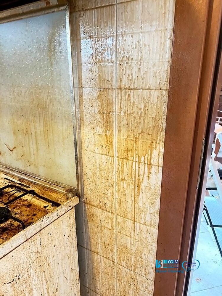 Parete e piano cottura della cucina sporchi e ricoperti di grasso e macchie marroni, con superfici di piastrelle che presentano forti accumuli e sporcizia vicino a una porta: un caso ideale per una soluzione di pulizia automatica Bozza.