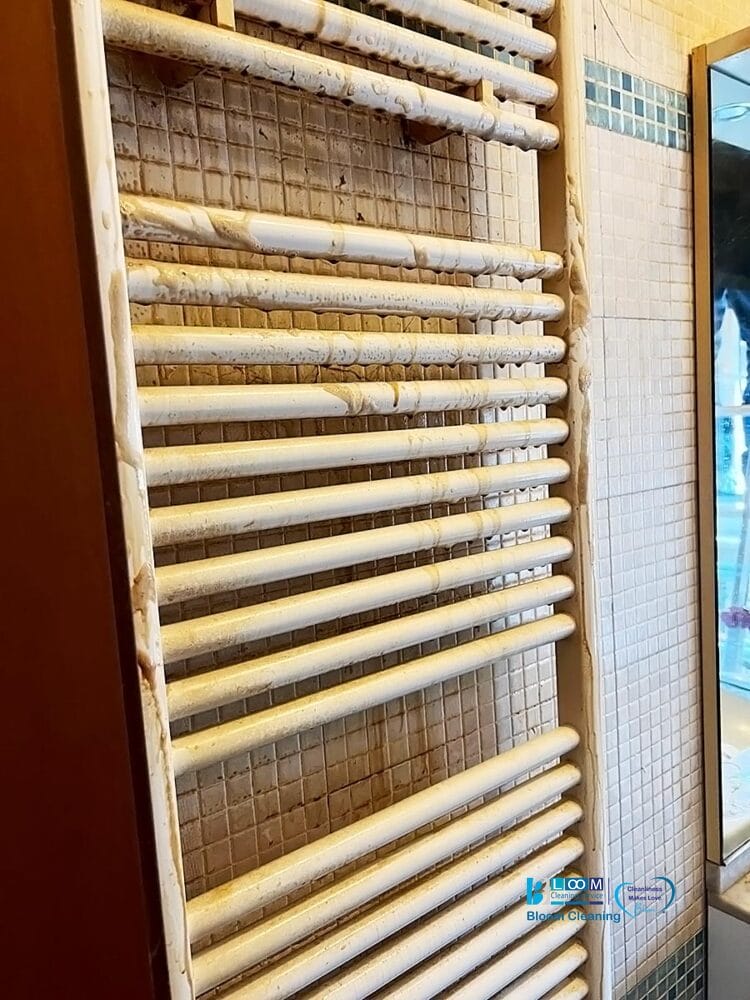 Uno scaldasalviette automatico Bozza coperto di residui di sapone secchi e schiumosi, montato su una parete piastrellata con uno specchio visibile sul lato destro.