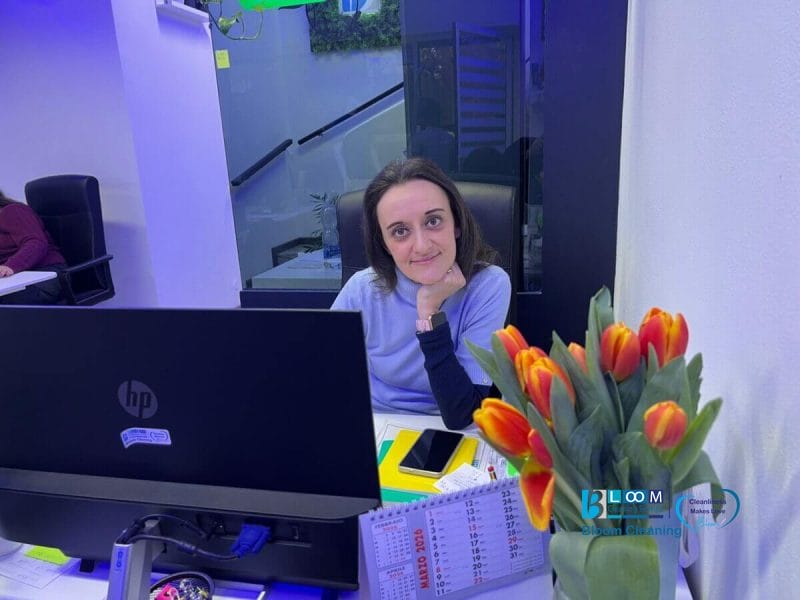 Una donna è seduta alla scrivania con un computer HP, guarda la telecamera e sorride dolcemente. In primo piano, sulla scrivania ci sono un mazzo di tulipani arancioni, un calendario e uno smartphone. L'ufficio è illuminato di blu.